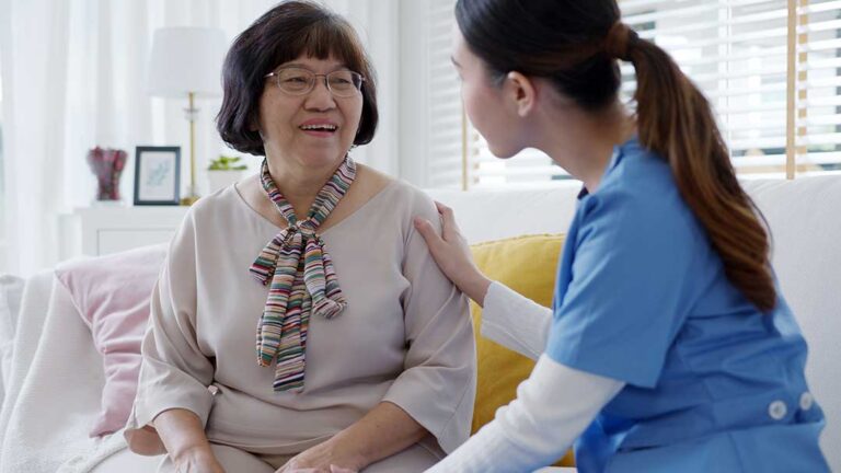 Adult child and older parent having a calm conversation at a kitchen table with notes nearby.
